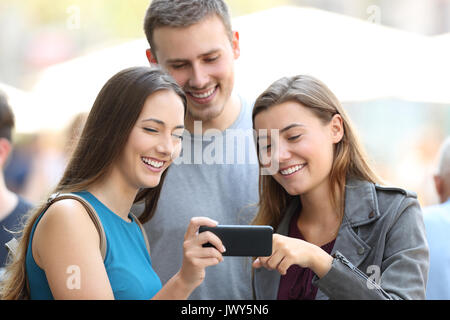 Drei glückliche Freunde Freigeben von Medien Inhalt mit einem Smart Phone auf der Straße Stockfoto