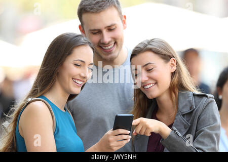 Drei Freunde, die Inhalte auf einem Smartphone stehen auf der Straße Stockfoto