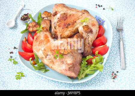 Zwei gebratene Hähnchenschenkel mit in Scheiben geschnittenen Tomaten auf einem blauen Schild. Stockfoto