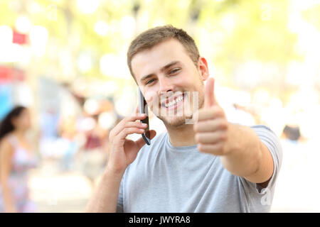 Vorderansicht Portrait von einem Kerl, der auf dem Telefon an Sie mit Daumen hoch auf der Straße Stockfoto