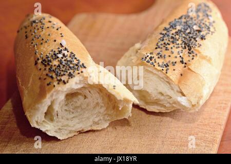 Zwei Stücke eines weißen Brötchen bestreut mit Mohn- und Salz auf einer hölzernen Schneidebrett. Stockfoto