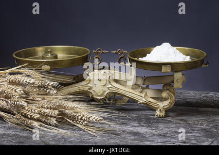 Vintage Küchenwaage mit Schaufel von Mehl stehen auf der alten hölzernen Schreibtisch. Das Bündel von Mais liegt im Vordergrund. Stockfoto