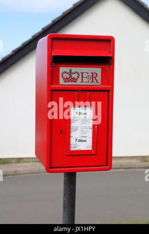 Eine ziemlich neue Post Box neben der Hauptstraße in einem Dorf mit seiner üblichen roten Anstrich und montiert auf einem Pfosten im Boden. Stockfoto