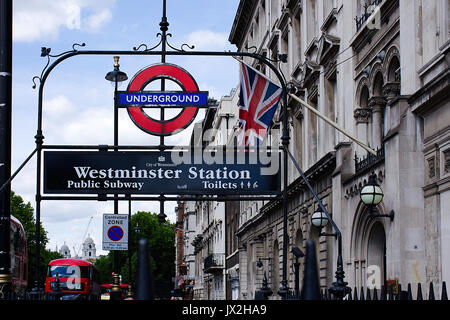 Westminster Station Eintrag, U-Bahn, Zeichen, Britische Flagge Gebäude blauer Himmel, Bäume, und roten Doppeldeckerbus im Hintergrund. Stockfoto