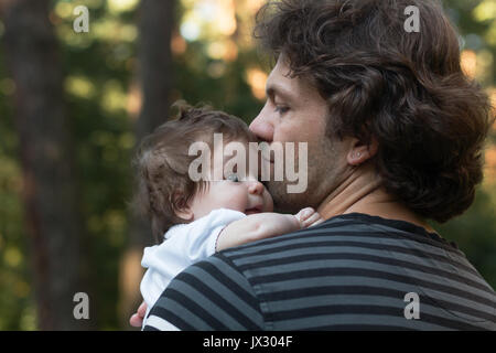Papa seinen kleinen blauäugige Tochter in seine Arme für einen Spaziergang im Park. Tag Sommer, Familie Natur zu Fuß, Sonnig Stockfoto