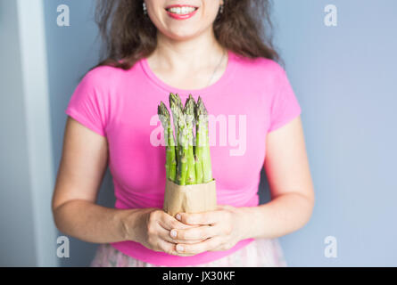 Weibliche Hand hält Bündel grüner Spargel. Konzept der Veganer, Vegetarier und gesunde Ernährung Stockfoto