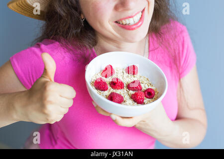 Frauenhand halten gesund und natürlich Frühstück, Haferflocken und Himbeeren in eine Schüssel geben Stockfoto
