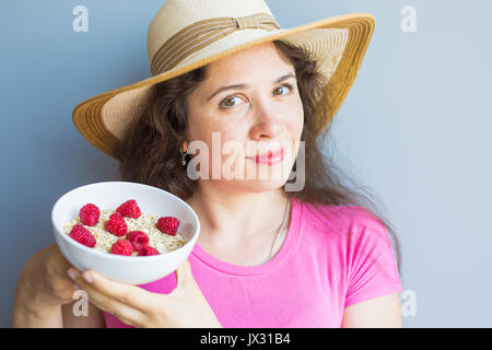 Lächelnde Frau halten gesund und natürlich Frühstück, Haferflocken und Himbeeren in eine Schüssel geben Stockfoto