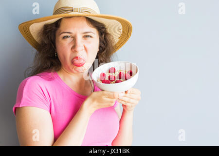 Lächelnde Frau halten gesund und natürlich Frühstück, Haferflocken und Himbeeren in eine Schüssel geben Stockfoto