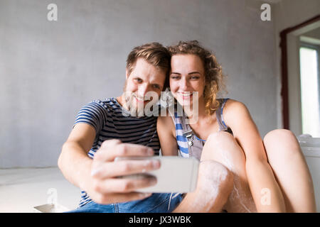 Schöne junge Paar in Liebe, Spaß, Malerei Mauern ihrer neuen Wohnung unter selfie mit Smart Phone. Home Makeover und Sanierungskonzept. Stockfoto