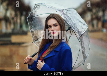 Portrait der junge schöne Mädchen versteckt sich unter einem Sonnenschirm von einem kleinen Regen. Ansicht des Modells ist an die Kamera gerichtet Stockfoto