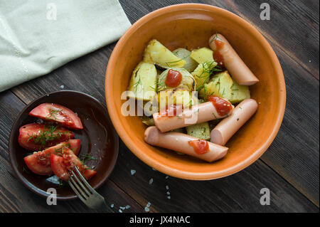 Brühwurst mit gebackenen Kartoffeln und frischen in Scheiben geschnittenen Tomaten auf einem Holztisch Stockfoto