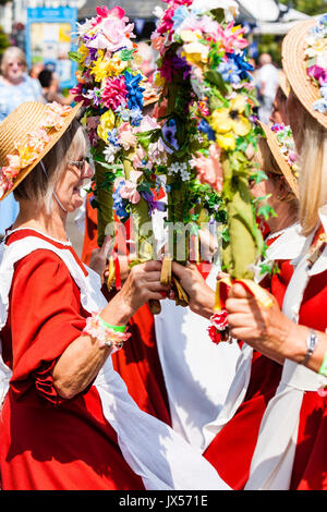 England, Broadstairs Folk Festival. Steigende Lerchen Morris Seite Tanzen draußen im hellen Sonnenschein mit Leute zu beobachten. Holding Halbkreis Girlanden aus Blumen, sie tragen orange Kleidern mit weißen Schürzen auf. Stockfoto