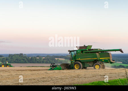 Green heavy Mähdrescher während des Abends in einem Feld während der Ernte im Sommer, England, Großbritannien Stockfoto