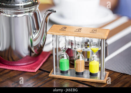 Metall Teekanne mit einer Sanduhr angezeigt, wenn drei verschiedene Arten von Tee einschließlich Weiß, Grün und Schwarz bereit sind. Braun Holz- Hintergrund. Stockfoto