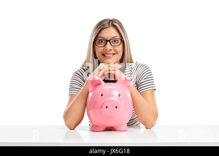 Junge Frau mit einem sparschwein an einem Tisch auf weißem Hintergrund sitzen Stockfoto