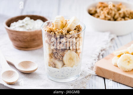 Chia pudding Parfait, mehrschichtige Joghurt mit Banane, Müsli. Gesundes Frühstück Konzept auf weissem Holztisch Stockfoto