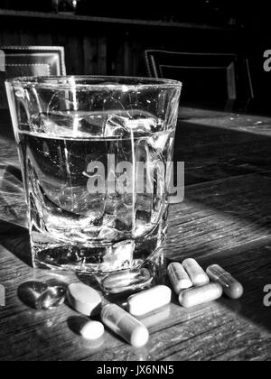 Schwarz-weiß Aufnahme der Vielzahl von Tabletten und ein Glas Wasser Stockfoto