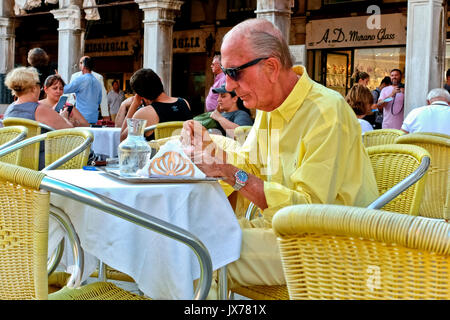 Ältere smart Gentleman in gelb Eis essen im Café im Freien mit gelben Stühle und Tischdecken gekleidet. Alter Mann. Markusplatz Venedig Italien Stockfoto