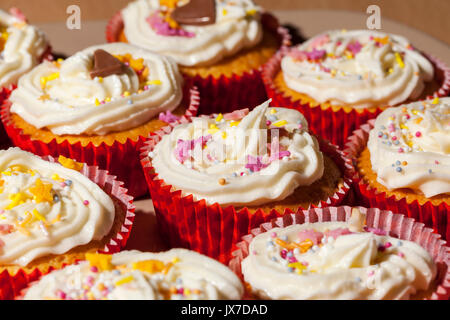 Teller mit frischen hausgemachten Kuchen im roten Büchsen gekrönt mit einem buttercream Wirbeln und Streuseln Stockfoto