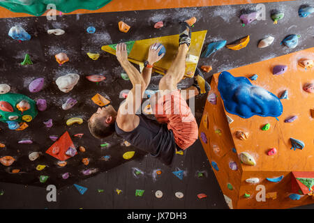 Junger Mann Bouldern in der Kletterhalle, versuchend, schwieriges Problem zu lösen Stockfoto