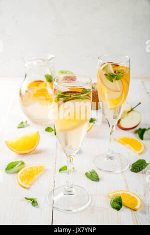 Getränke und Cocktails. Weiß herbst Sangria mit Apfel, Orange, Minze und Weißwein. In Gläser für Sekt, in einen Krug, auf einem weißen Holztisch. Stockfoto