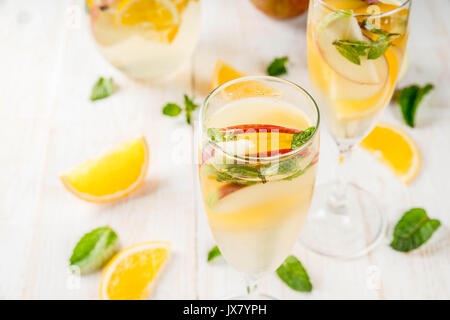 Getränke und Cocktails. Weiß herbst Sangria mit Apfel, Orange, Minze und Weißwein. In Gläser für Sekt, in einen Krug, auf einem weißen Holztisch. Stockfoto