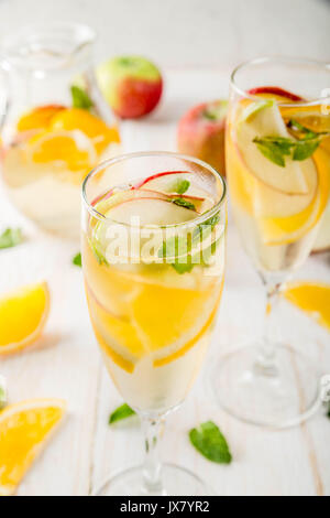 Getränke und Cocktails. Weiß herbst Sangria mit Apfel, Orange, Minze und Weißwein. In Gläser für Sekt, in einen Krug, auf einem weißen Holztisch. Stockfoto