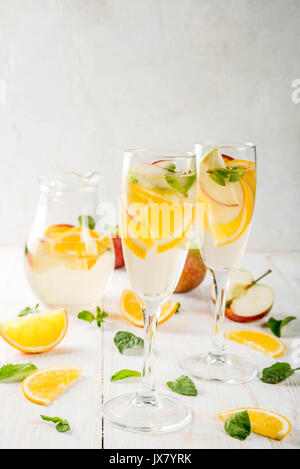 Getränke und Cocktails. Weiß herbst Sangria mit Apfel, Orange, Minze und Weißwein. In Gläser für Sekt, in einen Krug, auf einem weißen Holztisch. Stockfoto