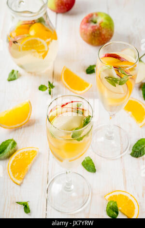 Getränke und Cocktails. Weiß herbst Sangria mit Apfel, Orange, Minze und Weißwein. In Gläser für Sekt, in einen Krug, auf einem weißen Holztisch. Stockfoto