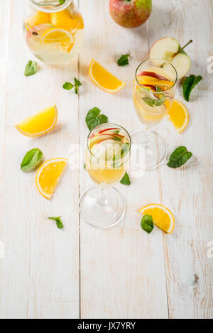 Getränke und Cocktails. Weiß herbst Sangria mit Apfel, Orange, Minze und Weißwein. In Gläser für Sekt, in einen Krug, auf einem weißen Holztisch. Stockfoto