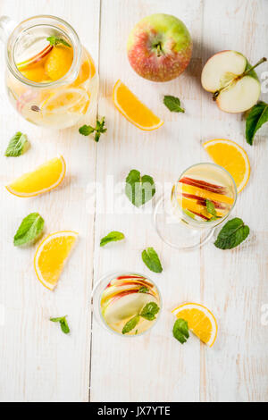 Getränke und Cocktails. Weiß herbst Sangria mit Apfel, Orange, Minze und Weißwein. In Gläser für Sekt, in einen Krug, auf einem weißen Holztisch. Stockfoto
