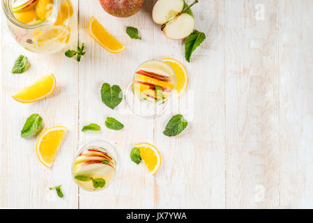 Getränke und Cocktails. Weiß herbst Sangria mit Apfel, Orange, Minze und Weißwein. In Gläser für Sekt, in einen Krug, auf einem weißen Holztisch. Stockfoto