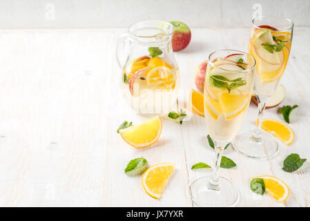 Getränke und Cocktails. Weiß herbst Sangria mit Apfel, Orange, Minze und Weißwein. In Gläser für Sekt, in einen Krug, auf einem weißen Holztisch. Stockfoto