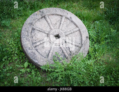Stein Granit Rad mit rostigem Metall rim auf grünem Gras isoliert Stockfoto