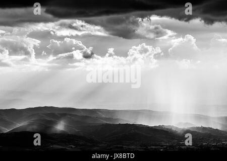 Spektakuläre Aussicht auf Sonne und Regen über einige Berge und Hügel, unter einem Moody und bewölkter Himmel Stockfoto