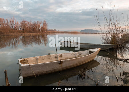 Einige kleine Fischerboote auf einem See an fast Sonnenuntergang, mit schönen Himmel und Wolken Reflexionen über noch Wasser Stockfoto