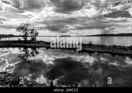 Ein Dock in einem See, mit einem schönen, tiefen Himmel mit Wolken auf dem Wasser spiegelt, zusammen mit ein paar Bäumen Stockfoto