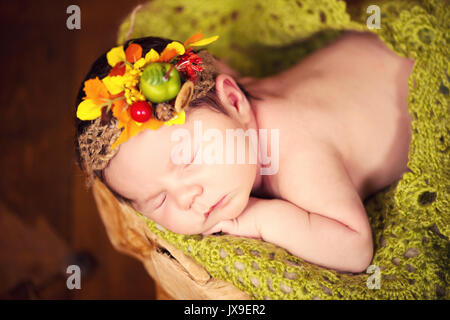 Ein neugeborenes Kind in einen Kranz von Kegeln und Beeren liegt auf einem Baumstumpf und schläft. Stockfoto