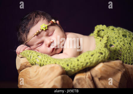 Ein neugeborenes Kind in einen Kranz von Kegeln und Beeren liegt auf einem Baumstumpf und schläft. Stockfoto