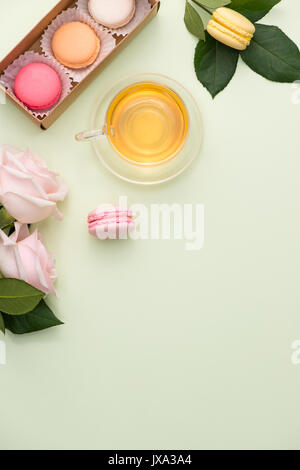 Französische Makronen. Viele süße bunte Macarons in Box mit Blumenstrauß aus Rosen auf dem Tisch Stockfoto