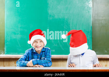 Zwei Jungen in santa Hüte Spaß haben gegen die Schule blackboard. Weihnachten Konzept Hintergrund mit Kopie Raum Stockfoto