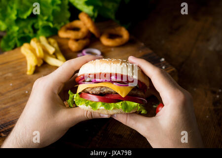 Cheeseburger. Man Hände Burger mit Käse, Zwiebeln, Tomaten, Salat grüner Salat und Gurken. Platz crop. Detailansicht, selektiver Fokus Stockfoto