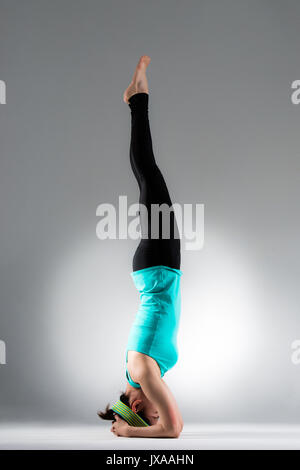 Junge weibliche Yoga-schüler Handstand auf den Boden und strecken die Beine in grauen Hintergrund. yoga Fitness Workout Body Concept. Stockfoto