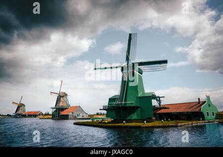 Panoramablick auf authentische Zaandam Mühlen in Zaanstad Dorf am Fluss Zaan gegen den stürmischen Himmel mit Wolken. Wahrzeichen der Niederlande. Stockfoto