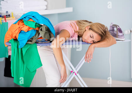 Junge Ermüdung Frau am Bügelbrett Neben Stapel von Kleidung zu Hause schlafen Stockfoto