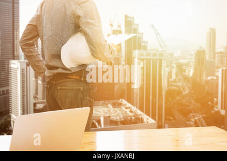 Builder Ingenieur holding Sicherheit Helm Blick auf blueprint Papier Fertigungszeichnung planen und Laptop Stockfoto