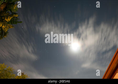 Nachthimmel mit Sternen, Mond und Wolken. Palmenblättern und Dach im Vordergrund. Stockfoto