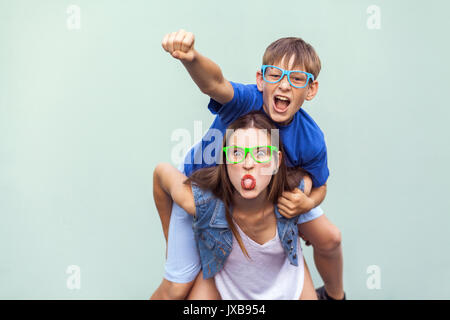 Crazy Emotionen und Gefühle. Super mann Stil! Die sommersprossige Bruder kletterte bis auf der Rückseite der älteren netten Schwester. Sie lustig, verrückt, im Gesicht, der Zunge, Stockfoto