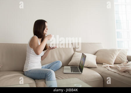 Junge Frau genießen Kaffee auf Sofa mit Laptop, Tag Stockfoto